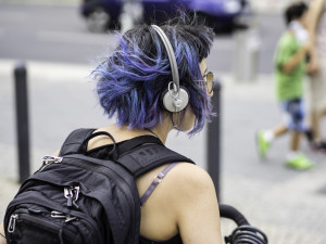 Frau mit blauen Haaren und Kopfhörerern und einem Rucksack auf dem Rücken.